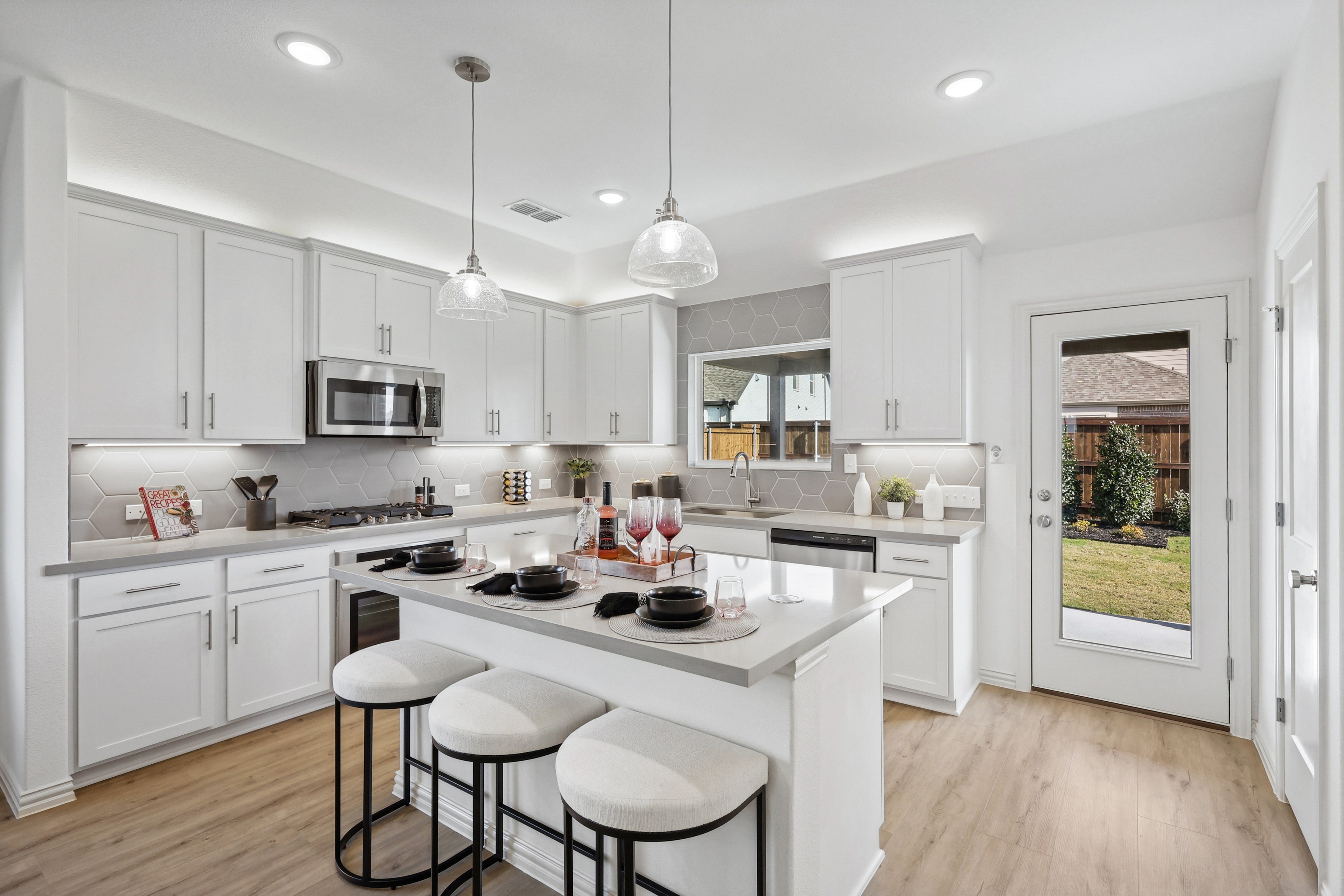 Modern kitchen in Bel Air Village; white cabinets, hex tile backsplash, island with stools, glass pendant lights.
