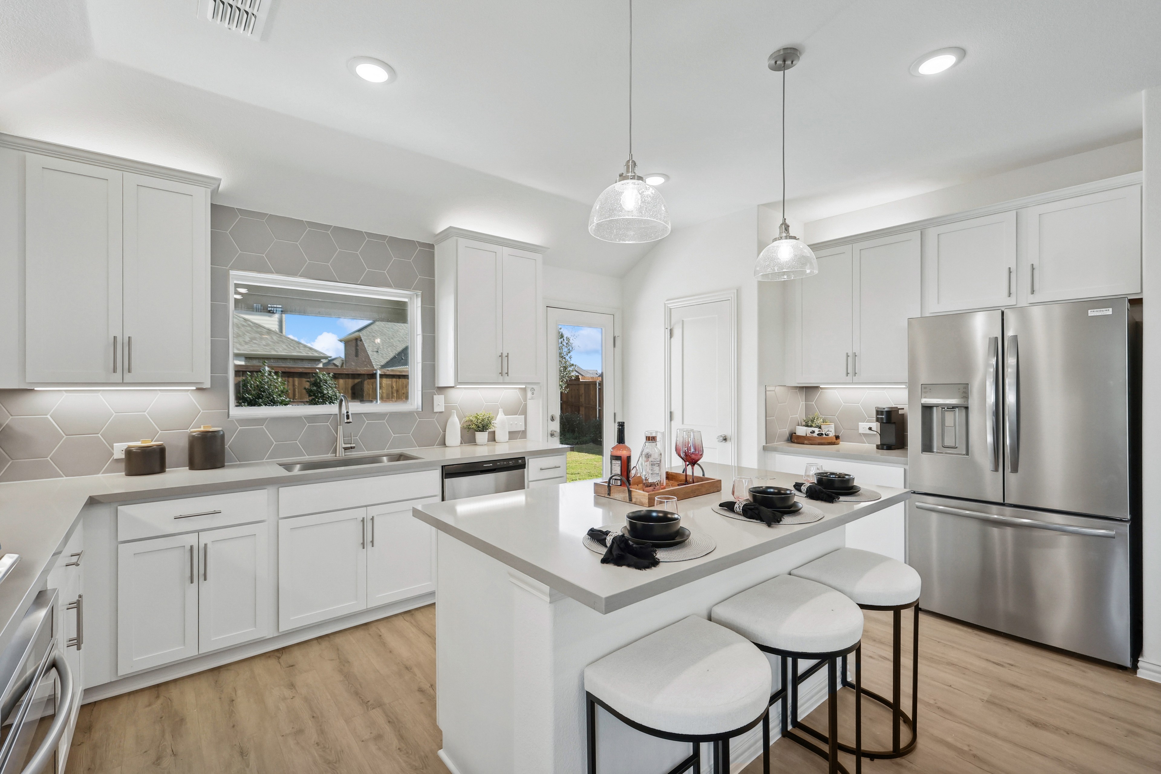 Modern Bel Air Village kitchen with white cabinets, hex tile backsplash, island, pendant lights, stainless appliances.