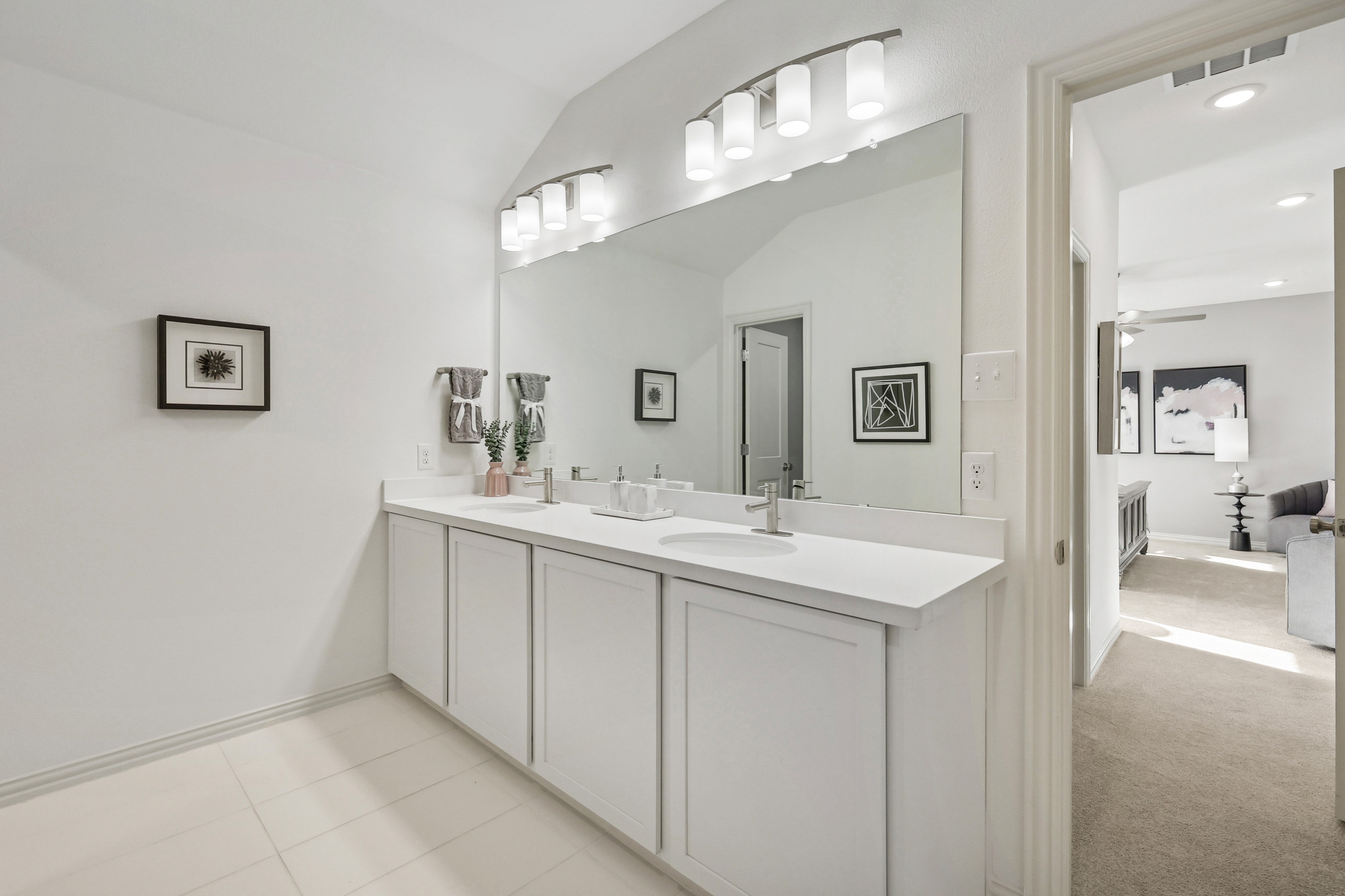 Elegant white bathroom with dual sinks and large mirror in Bel Air Village. Modern lighting, framed art on walls.