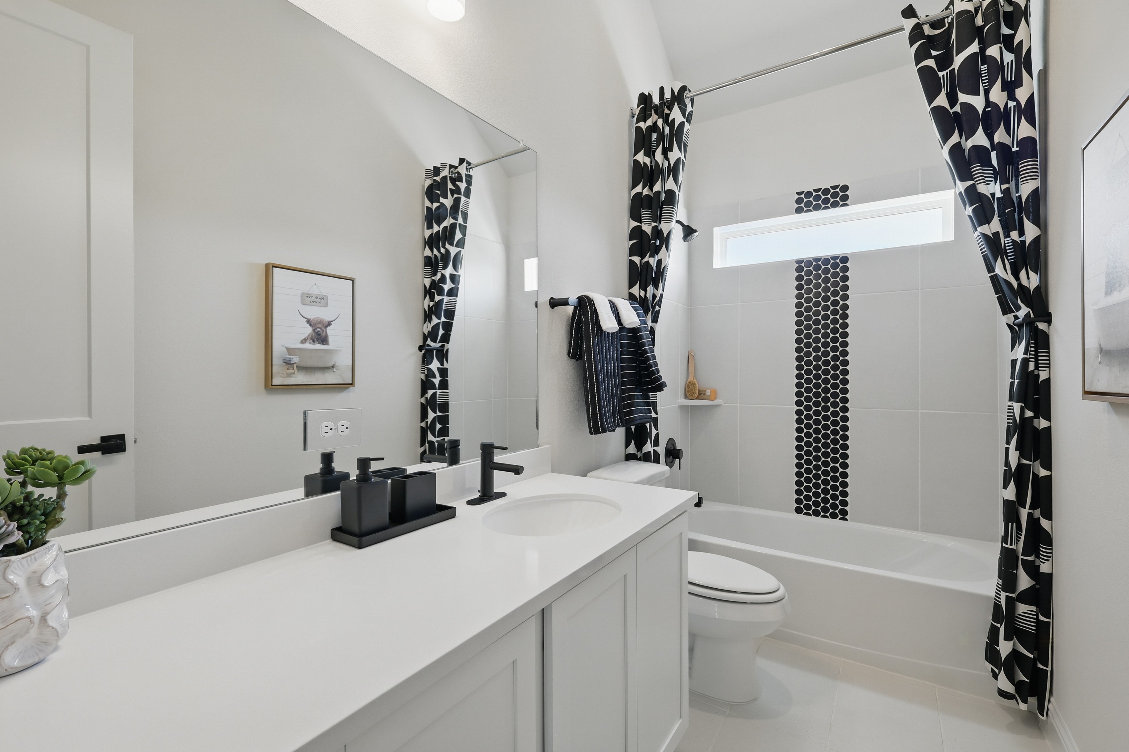 Modern bathroom with black fixtures, geometric curtains, sleek countertop, vertical window. Green Oaks Preserve.
