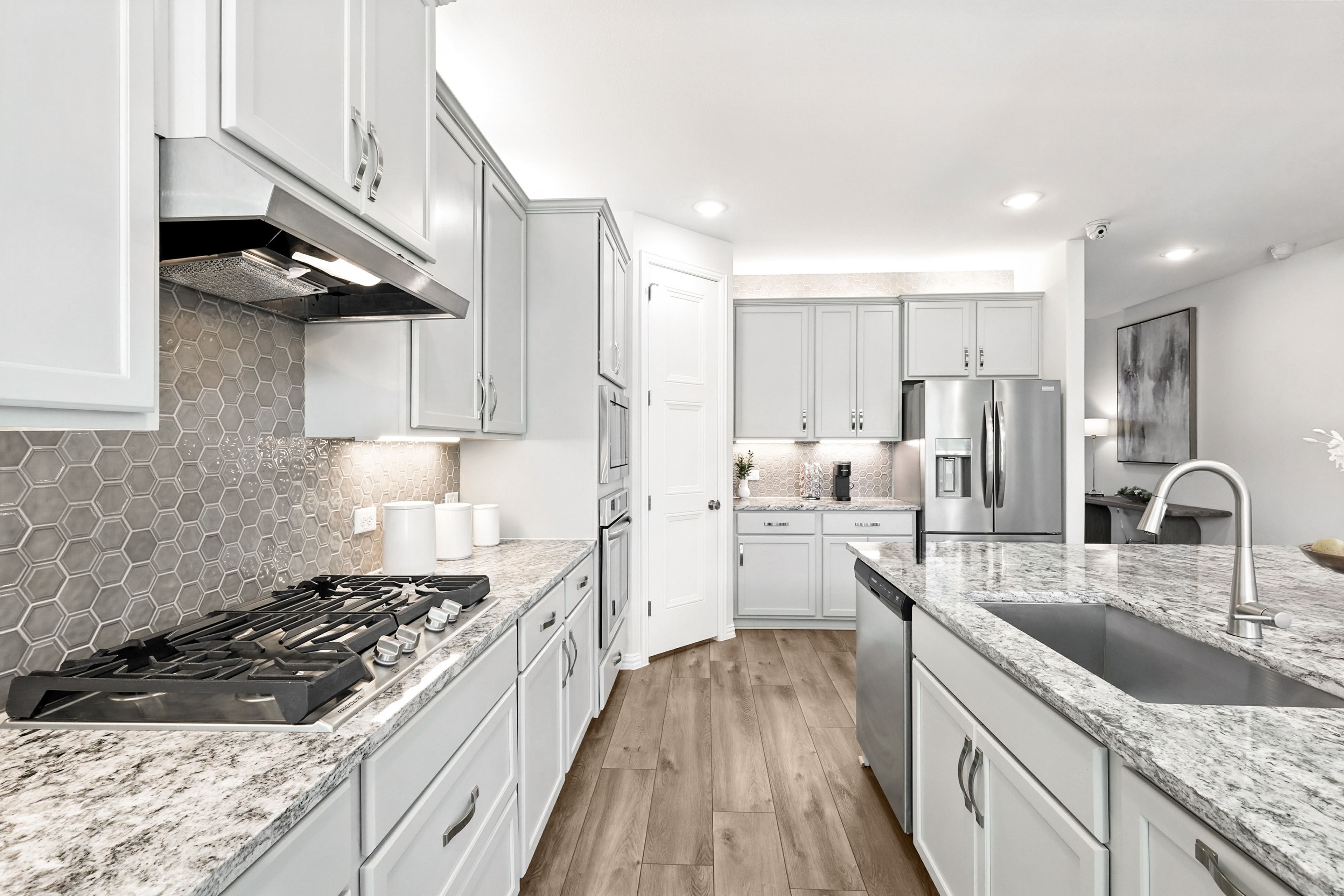Modern kitchen with white cabinetry, hexagonal backsplash, granite countertops, and stainless appliances in Green Oaks Preserve.