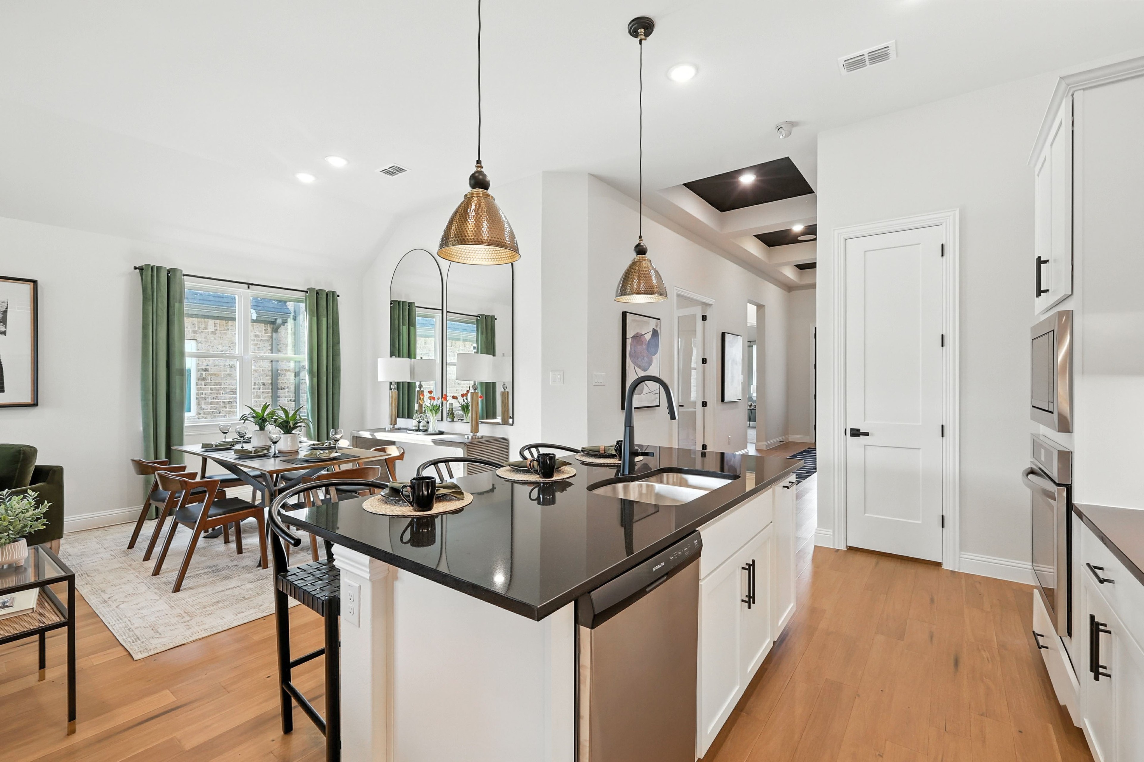 Modern kitchen-dining area with black countertops, pendant lights, hardwood floors in Green Oaks Preserve home.