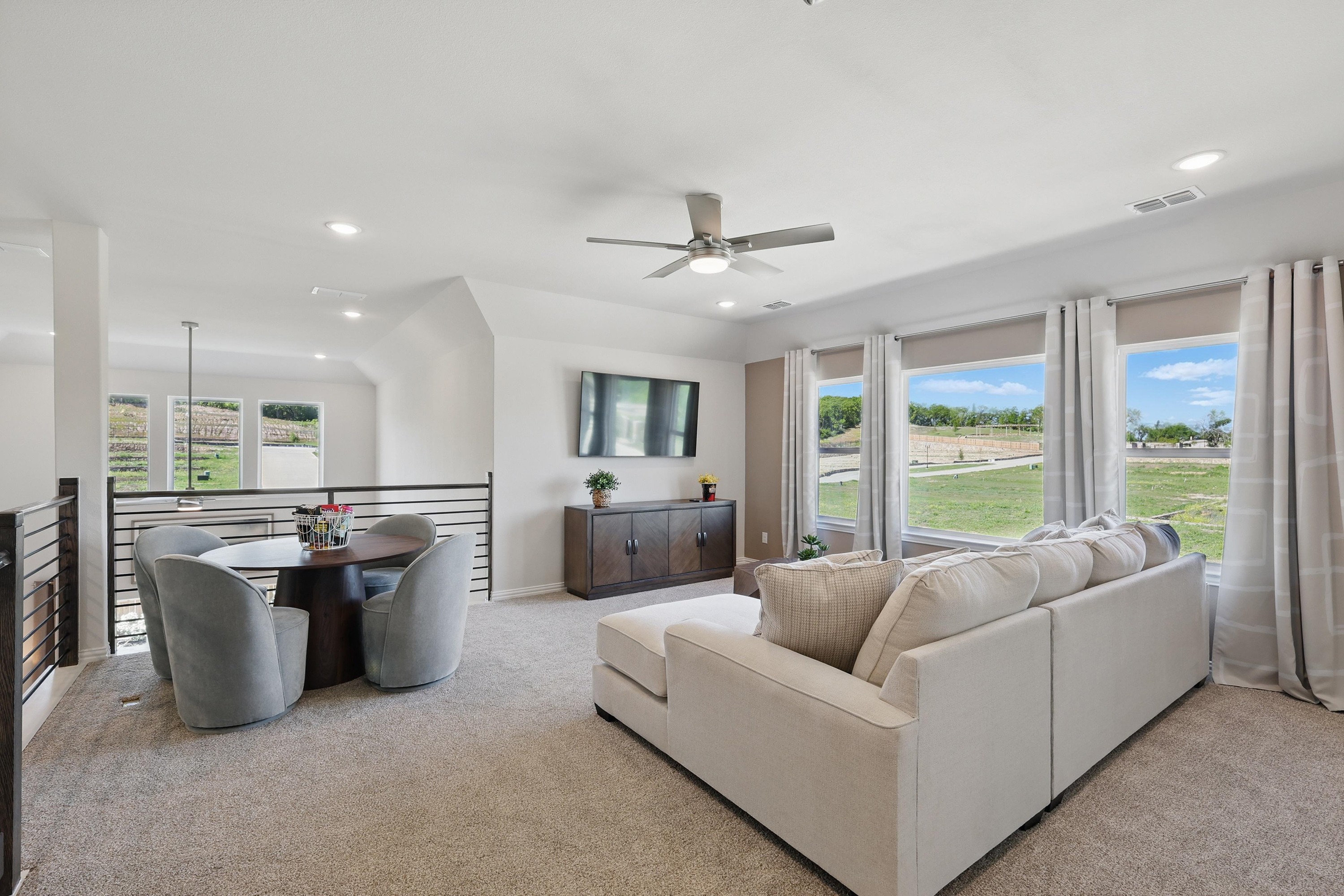 Spacious modern living room with ceiling fan, large windows, plush carpet in Green Oaks Preserve community.