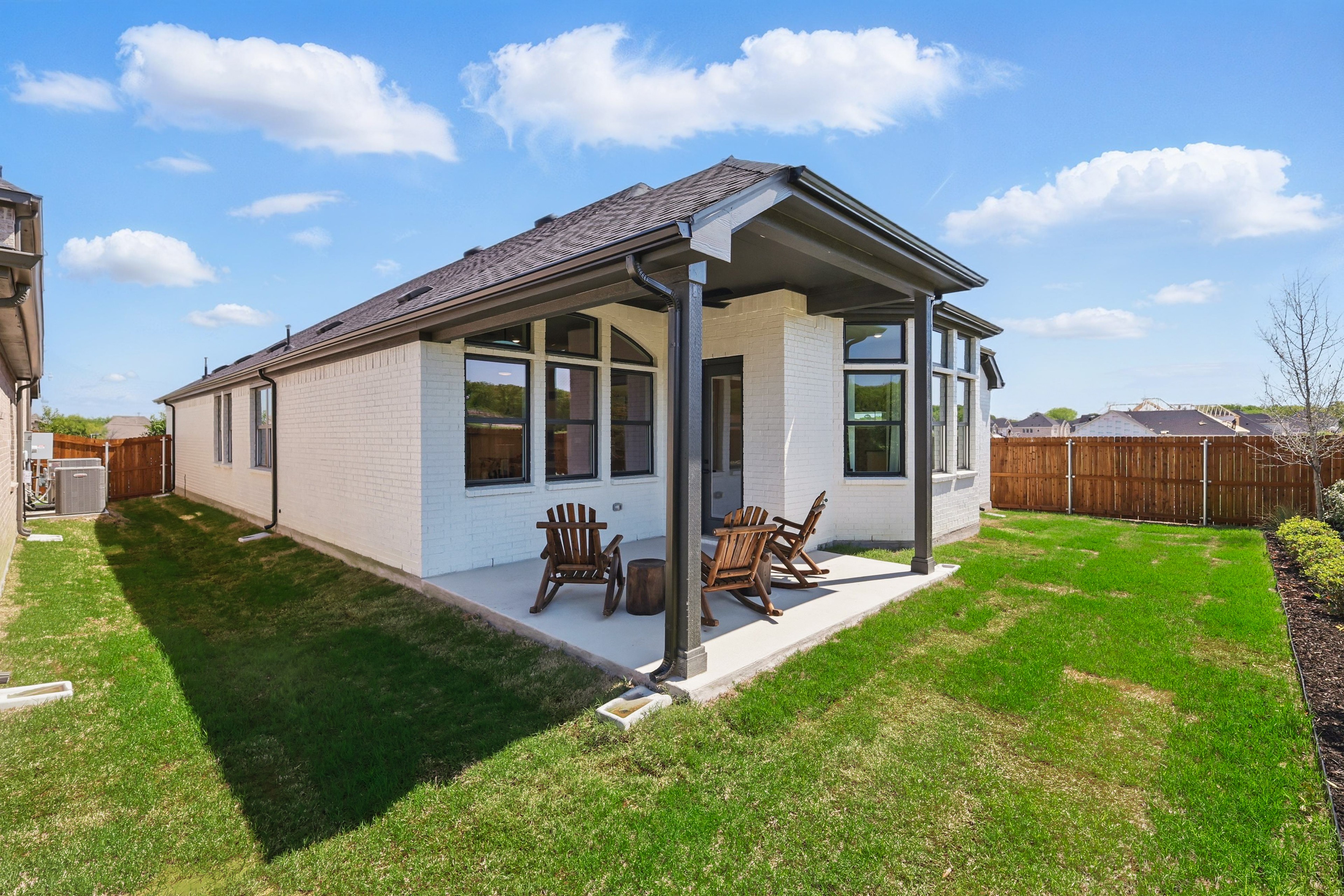 White brick house with gable roof, patio, wooden chairs, fenced yard, in Green Oaks Preserve community.