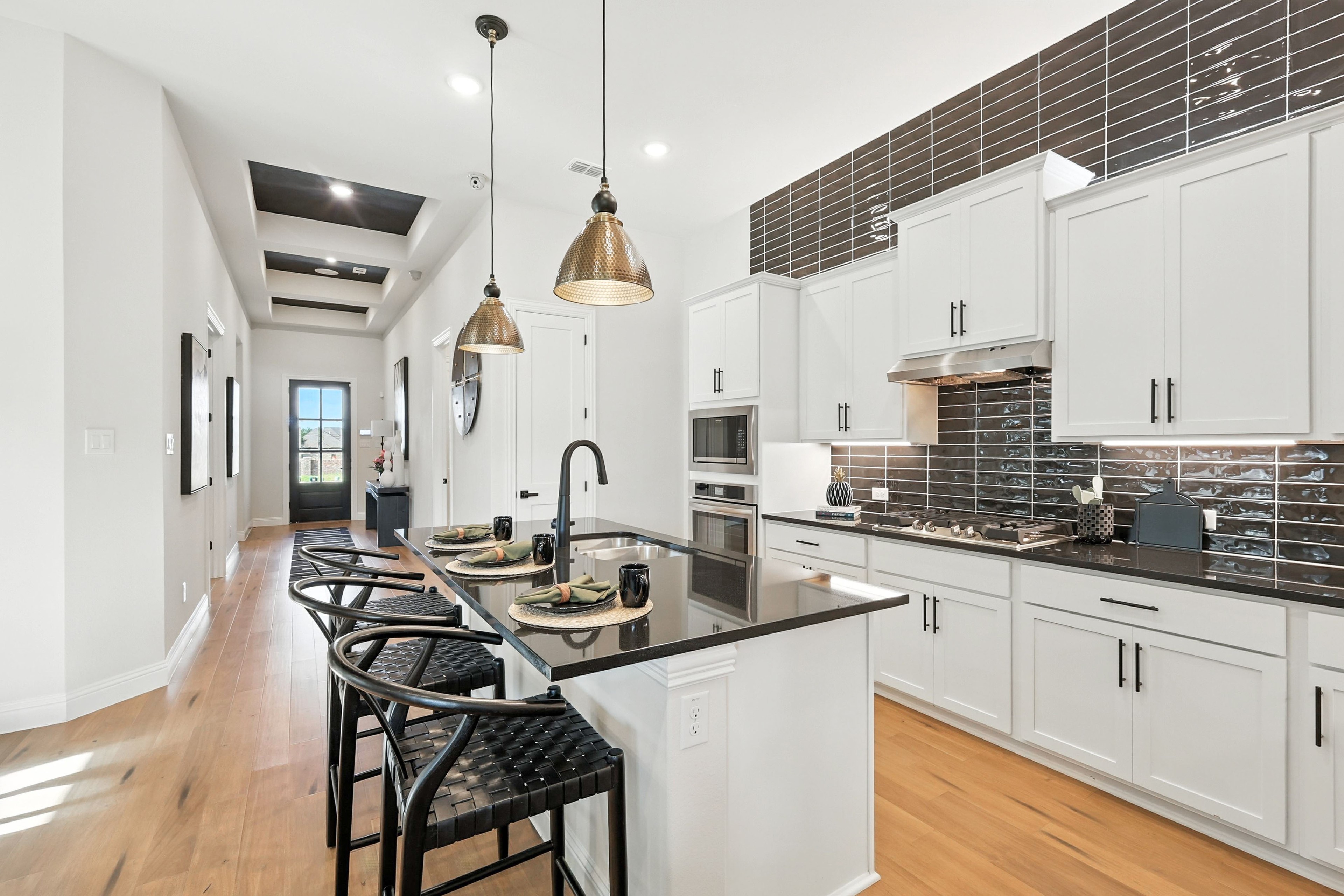 Modern kitchen in Green Oaks Preserve; white cabinets, black granite counters, wood floor, pendant lights.