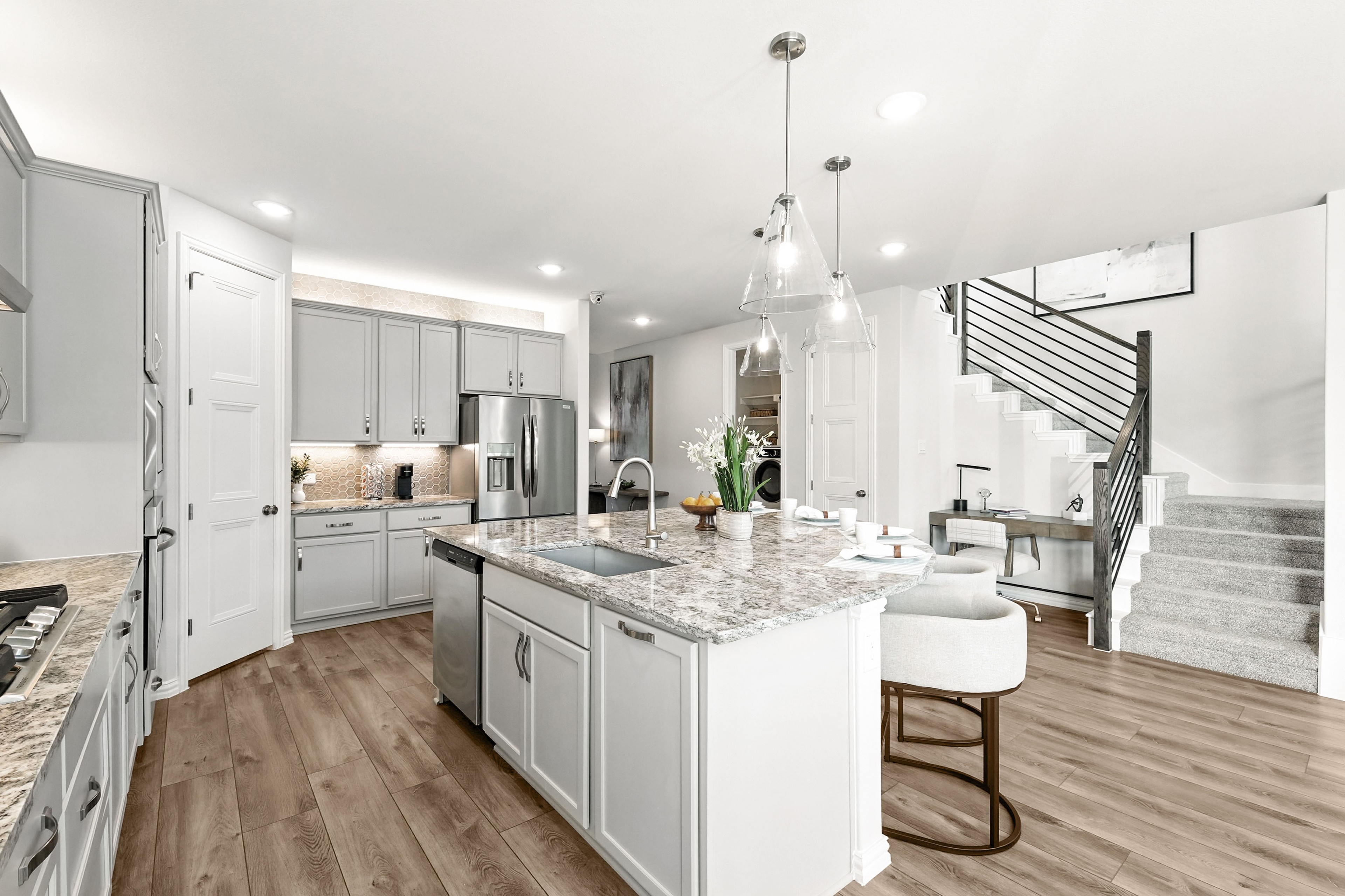Modern kitchen with marble island, wood floors, elegant lighting, and staircase, Green Oaks Preserve.