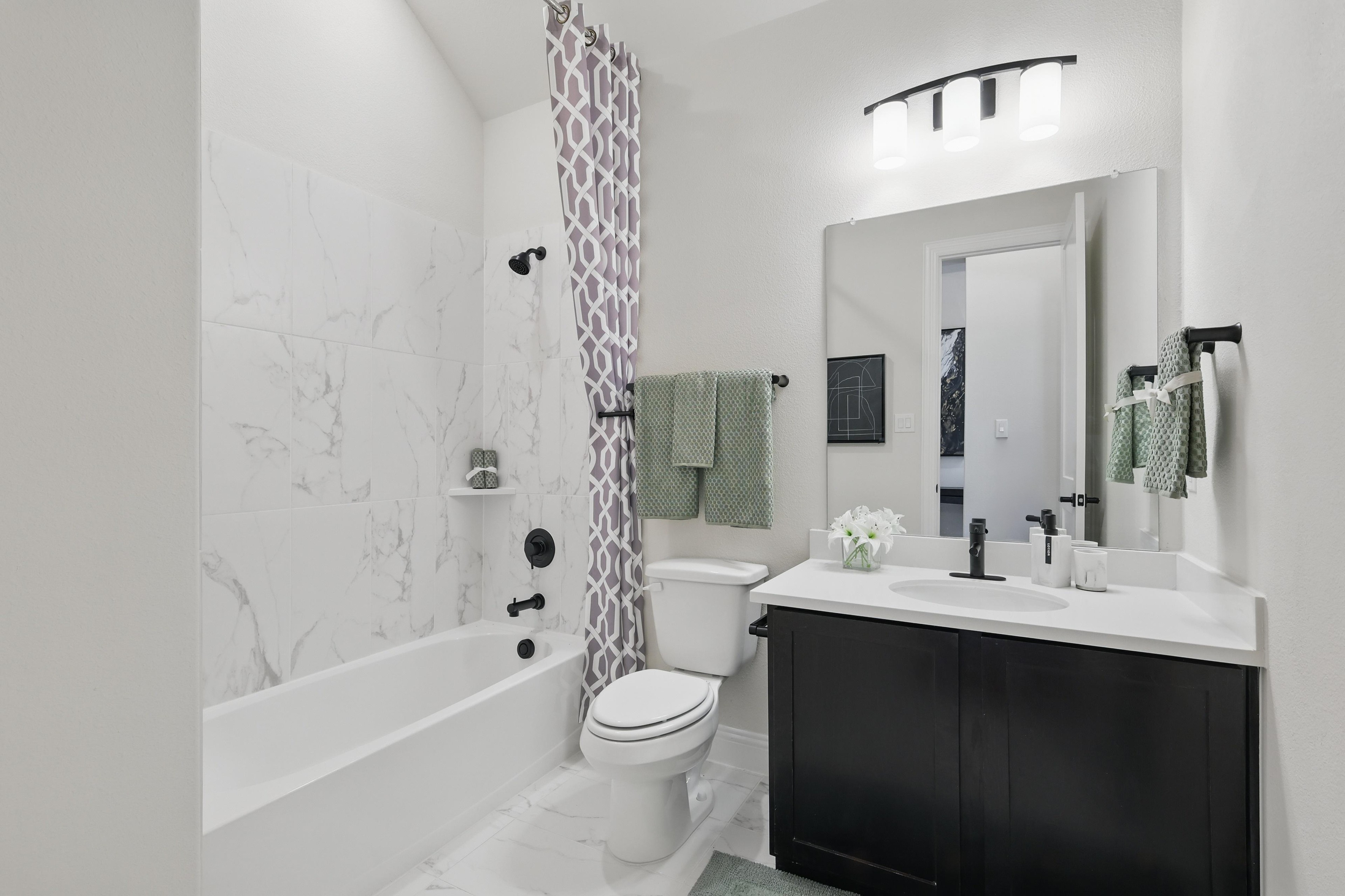 Modern bathroom with marble tiles, black fixtures, and large mirror in Green Oaks Preserve community.