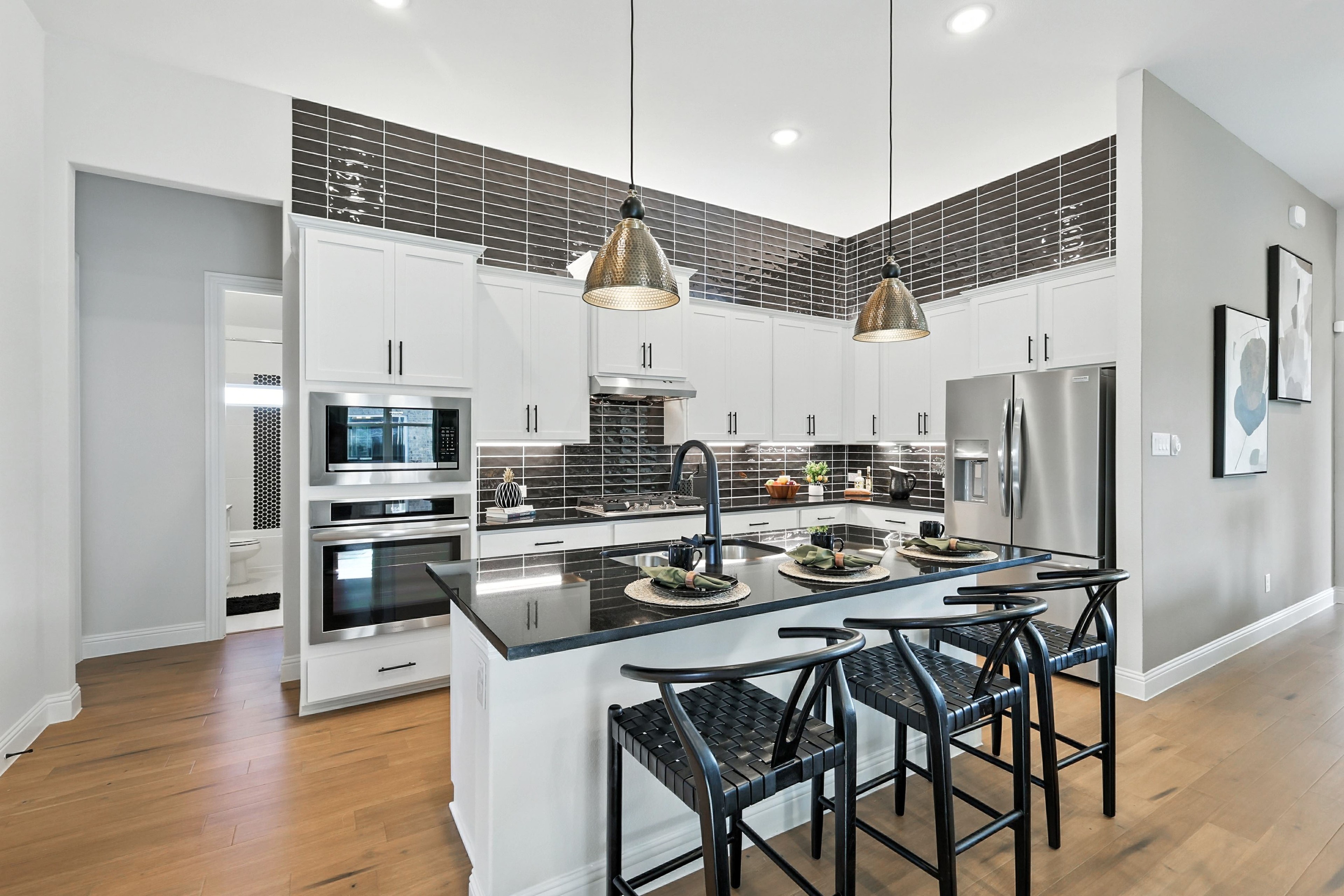 Modern kitchen with white cabinets, black countertops, pendant lights. Green Oaks Preserve luxury real estate.