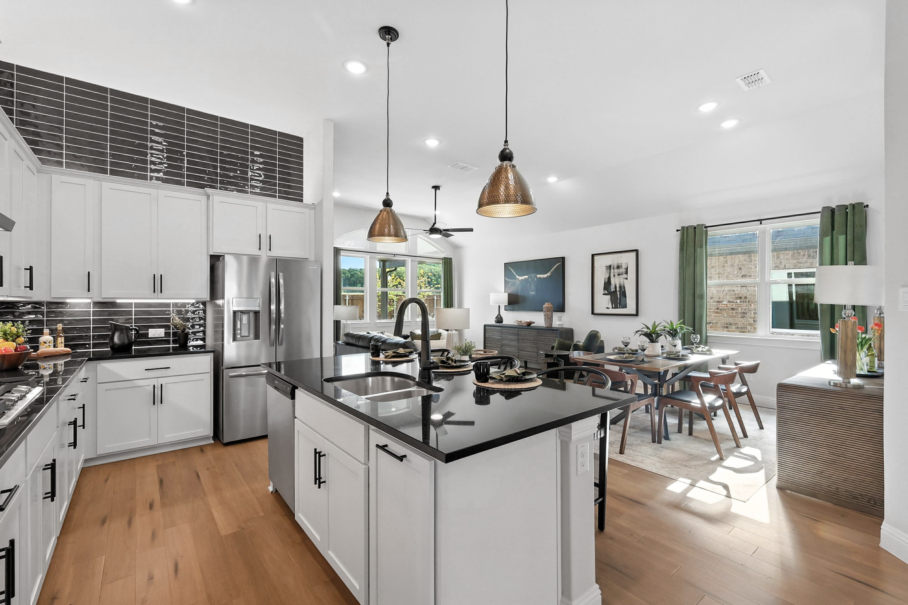Modern kitchen in Green Oaks Preserve, featuring white cabinetry, black countertops, open floor plan, and pendant lighting.