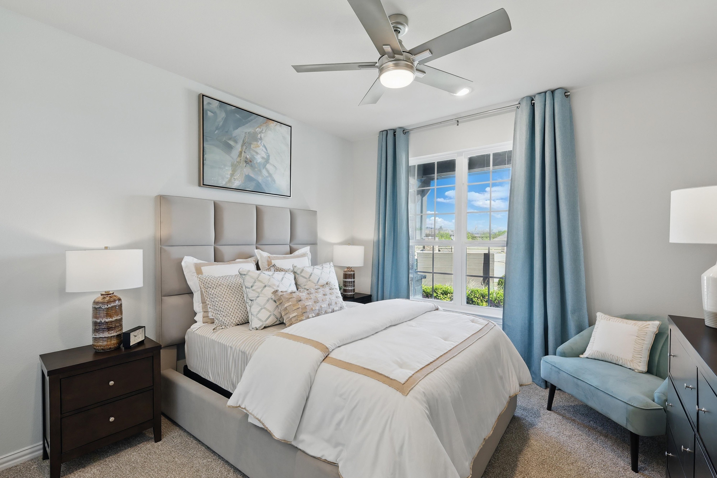 Elegant bedroom in Green Oaks Preserve with king bed, blue curtains, and modern ceiling fan. Large window offers garden view.