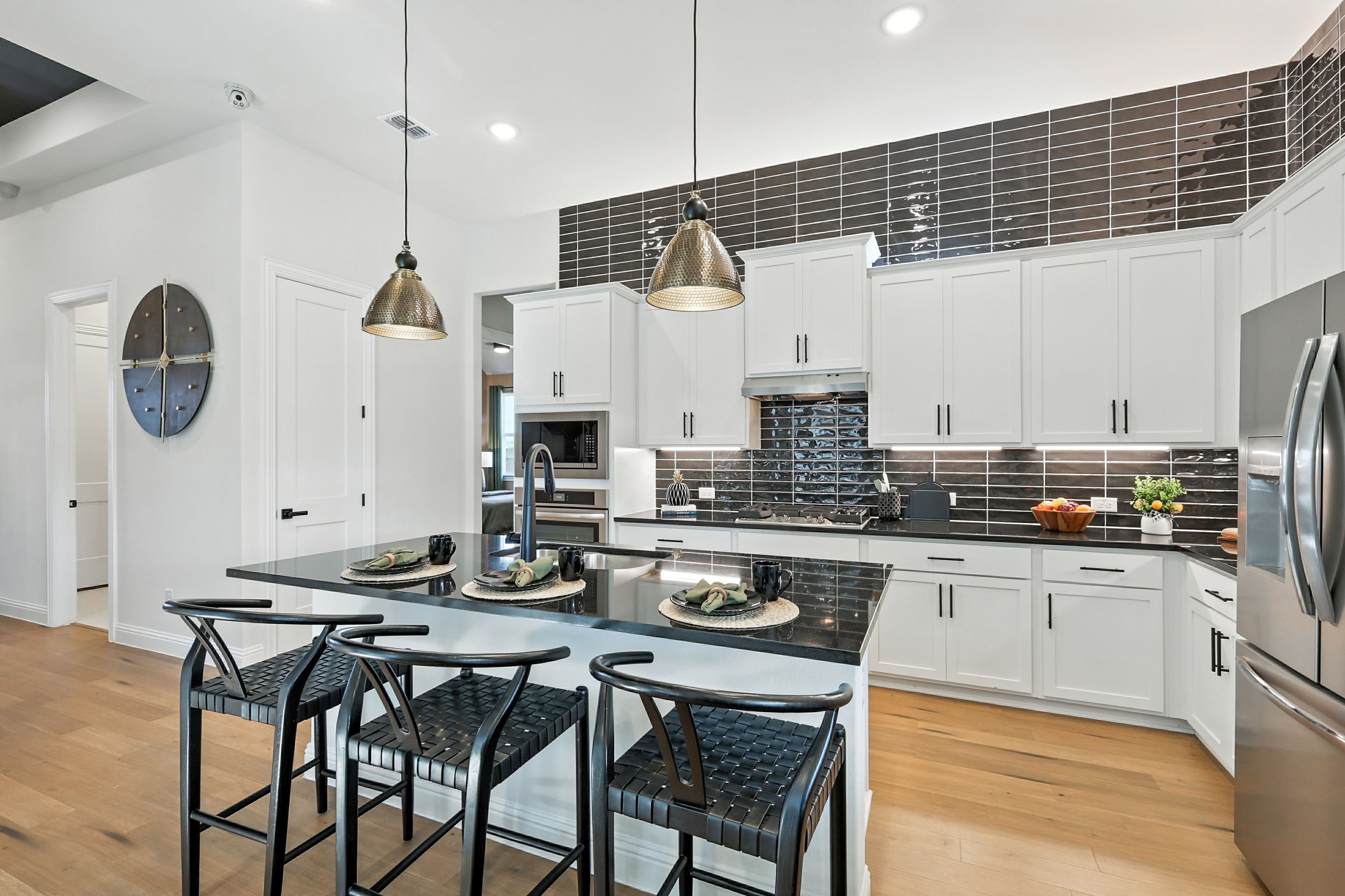 Modern kitchen with white cabinets, black tile backsplash, pendant lights, in Green Oaks Preserve.