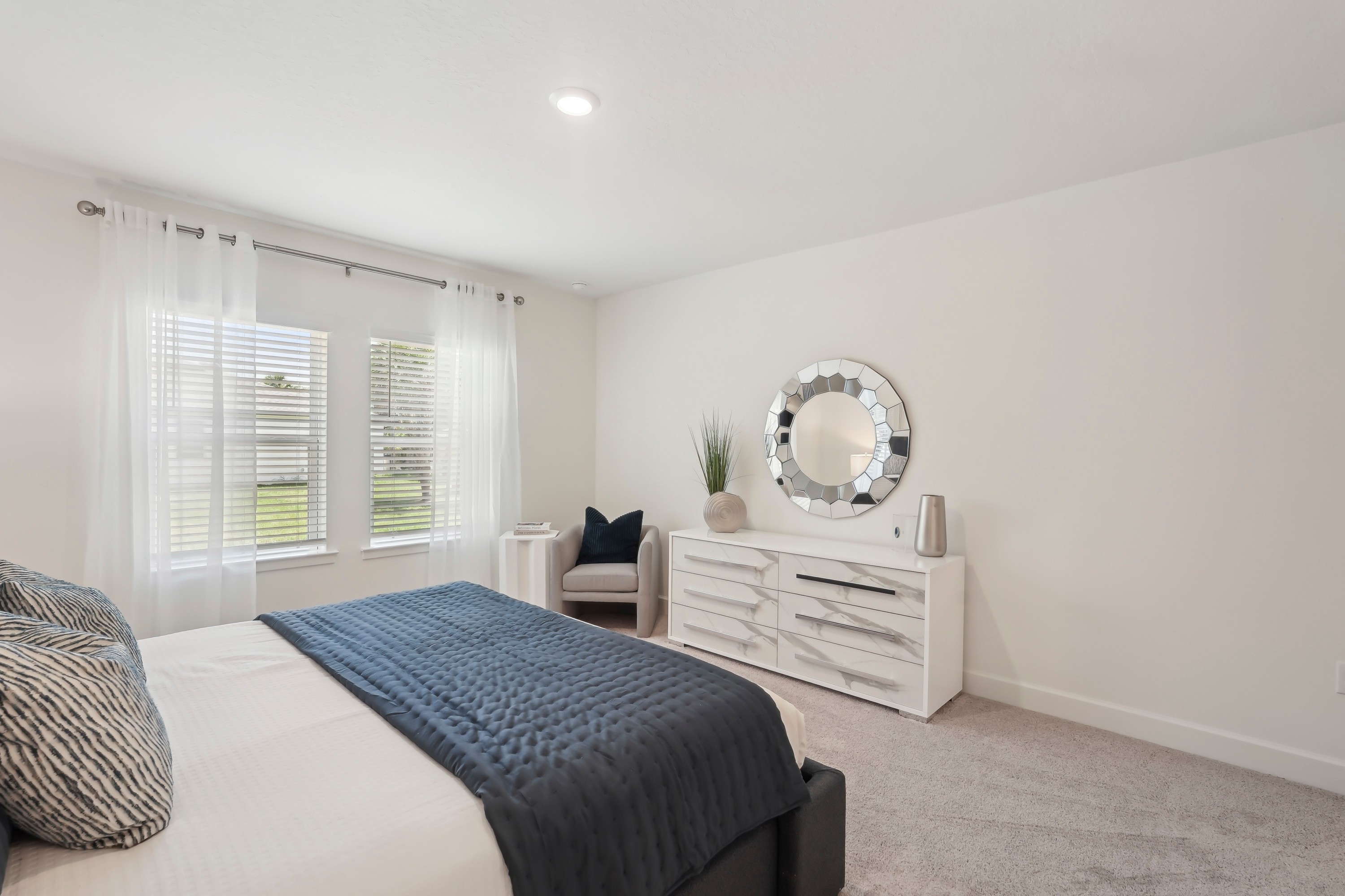 Bright North Port bedroom with white dresser, round mirror, and large windows.