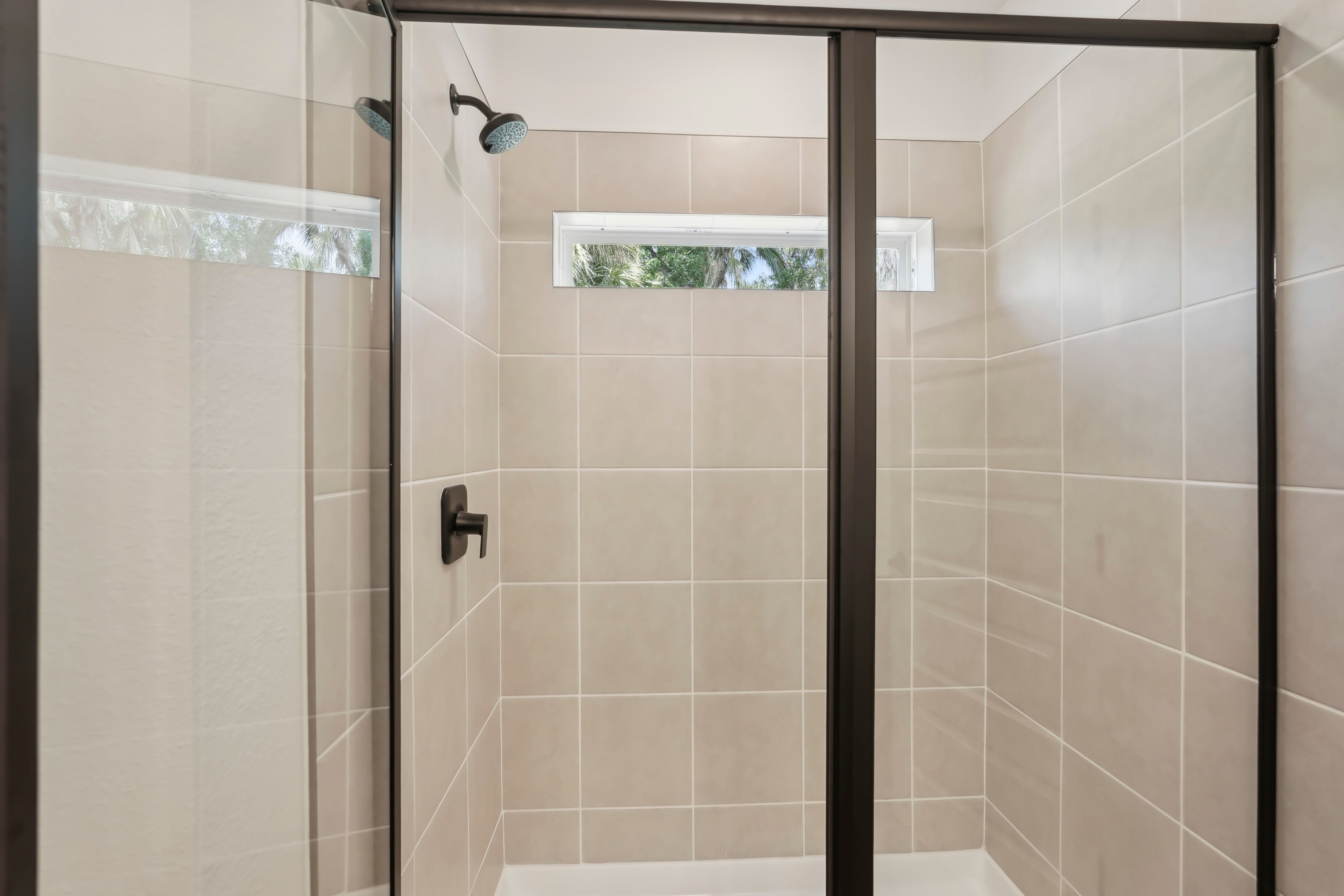 Modern shower with glass door, tiled walls, and sleek fixtures in North Port home.