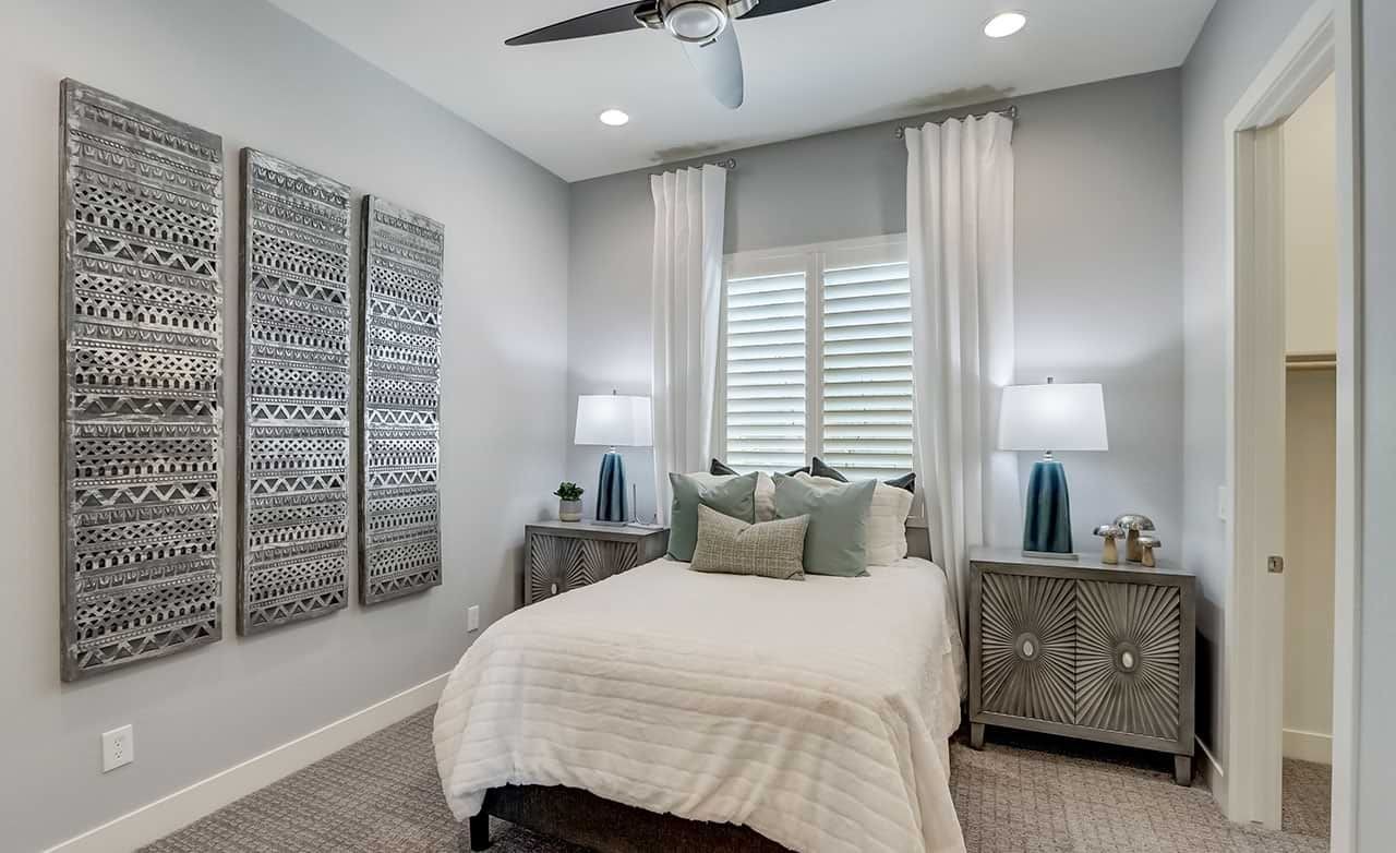 Modern bedroom in Hacienda, featuring textured wall art, dual nightstands, and ceiling fan. Neutral palette.