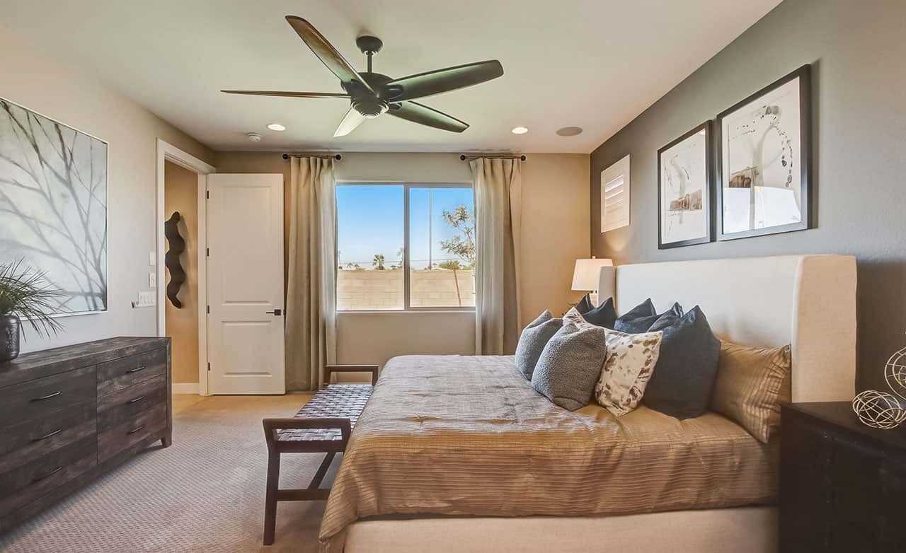 Modern bedroom with beige decor, ceiling fan, large window, and contemporary art at Castillo, Anderson Parc, Arizona.