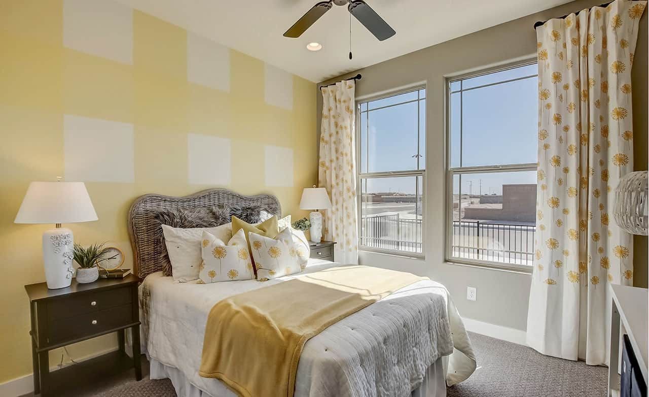 Cozy bedroom with wicker headboard, yellow accents, large windows, floral curtains at Castillo at Anderson Parc.