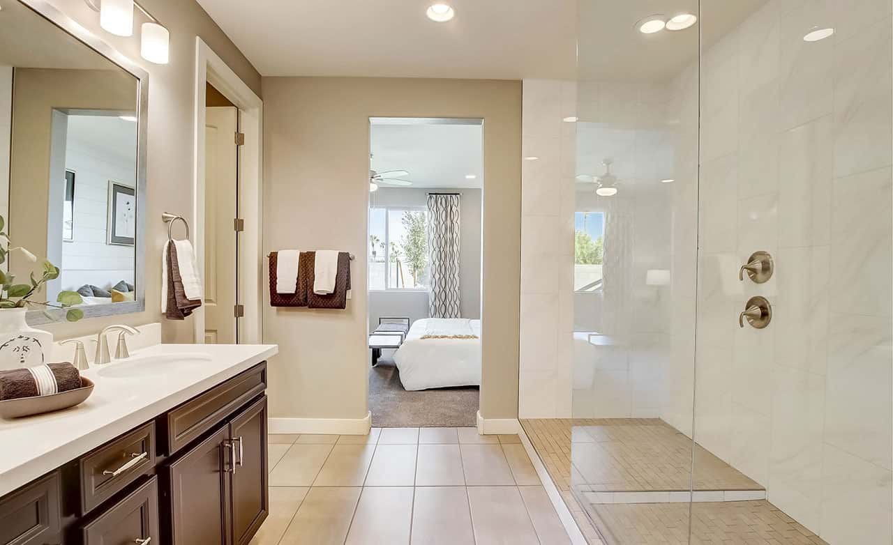 Luxurious bathroom with double vanity, glass shower, and glimpse of bedroom at Castillo, Anderson Parc.