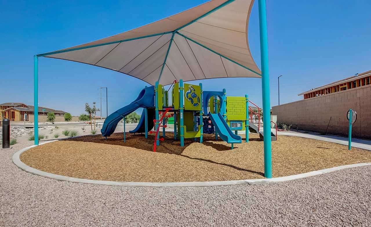 Vibrant playground with shade sail at Castillo at Anderson Parc, surrounded by new homes under construction.