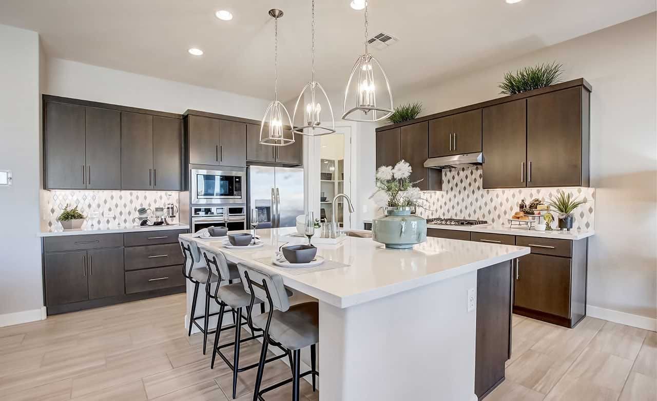 Modern kitchen at Mirada Crossing; dark cabinets, island, pendant lights, stainless appliances, tile backsplash.