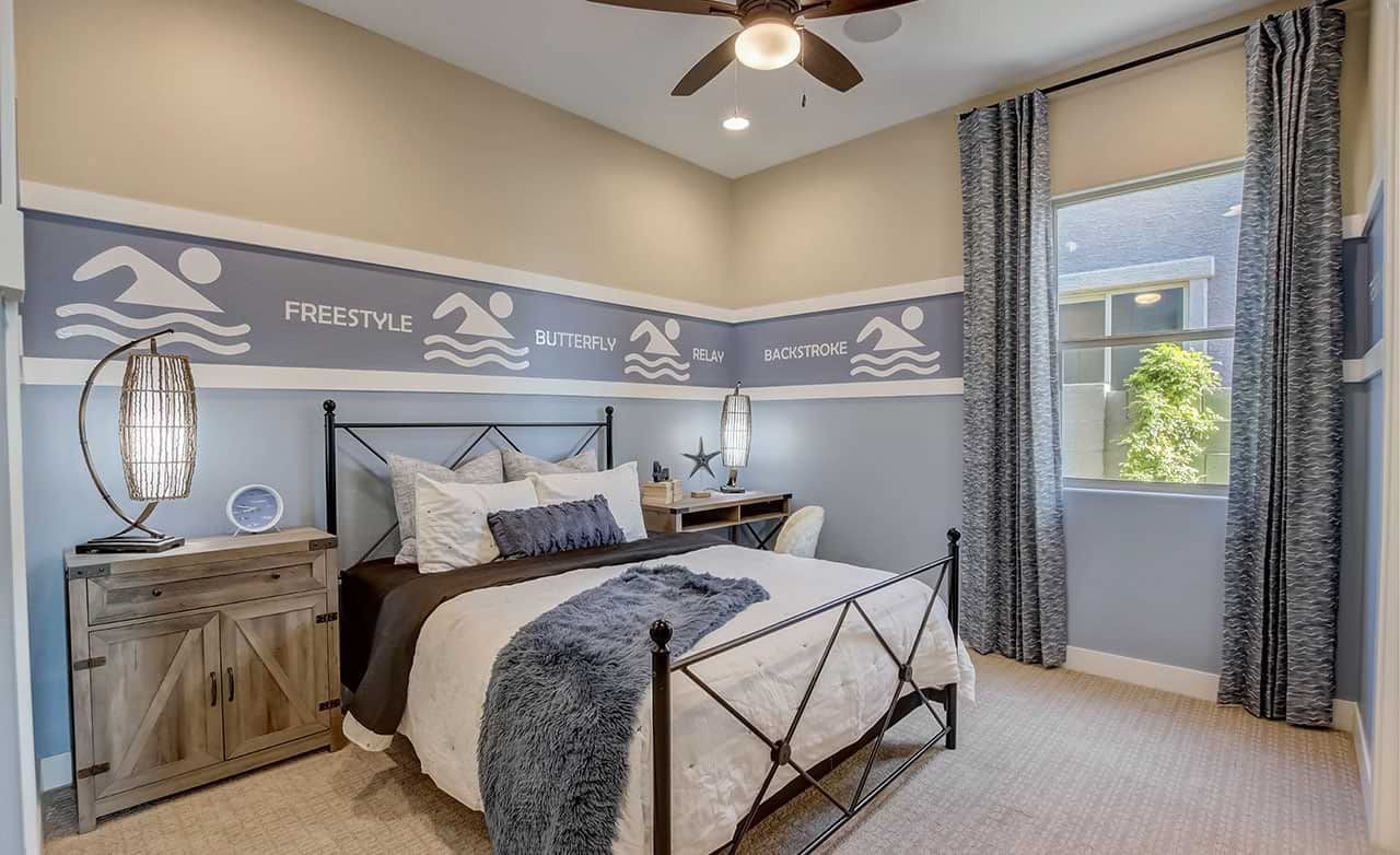 Bedroom with swim-themed decor, wrought iron bed, ceiling fan, and large window. Mirada Crossing community.