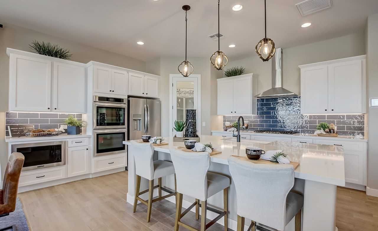 Modern kitchen with white cabinets, blue tile backsplash, and island seating. Located in Mirada Crossing, highlights elegance.