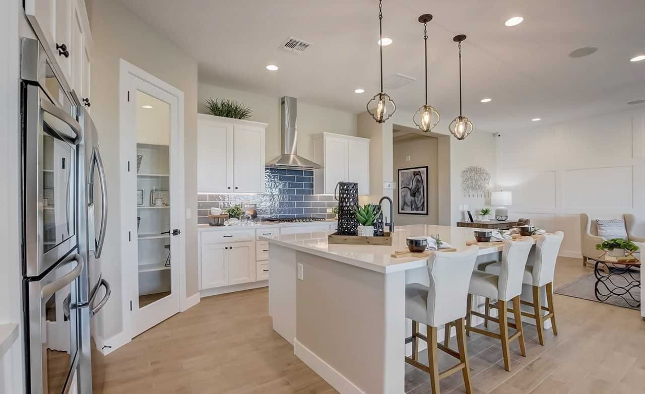 Modern kitchen with white cabinets, island, pendant lights, and stainless steel appliances in Mirada Crossing.