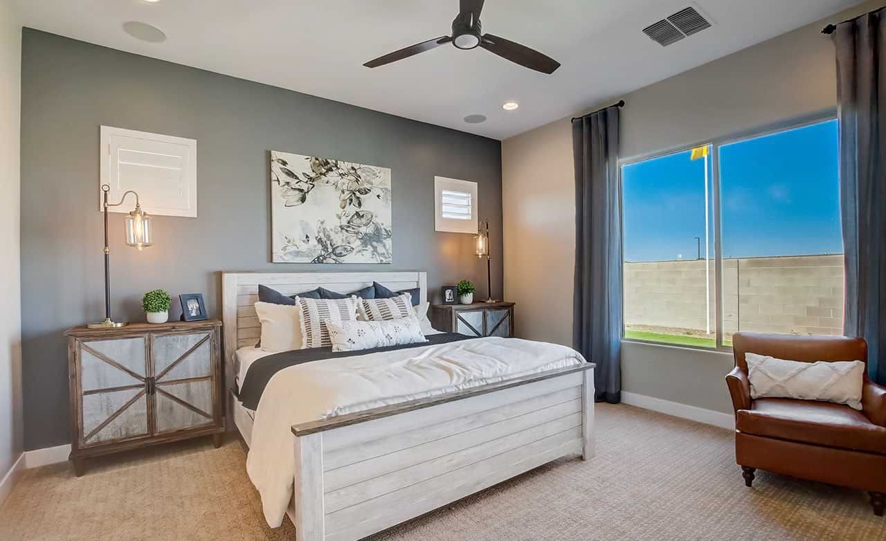 Elegant bedroom with gray accent wall, modern ceiling fan, large window. Mirada Crossing, contemporary furniture.