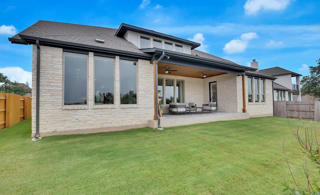 Modern stone home with large windows, covered patio, lush lawn in Oaks at San Gabriel, Texas.