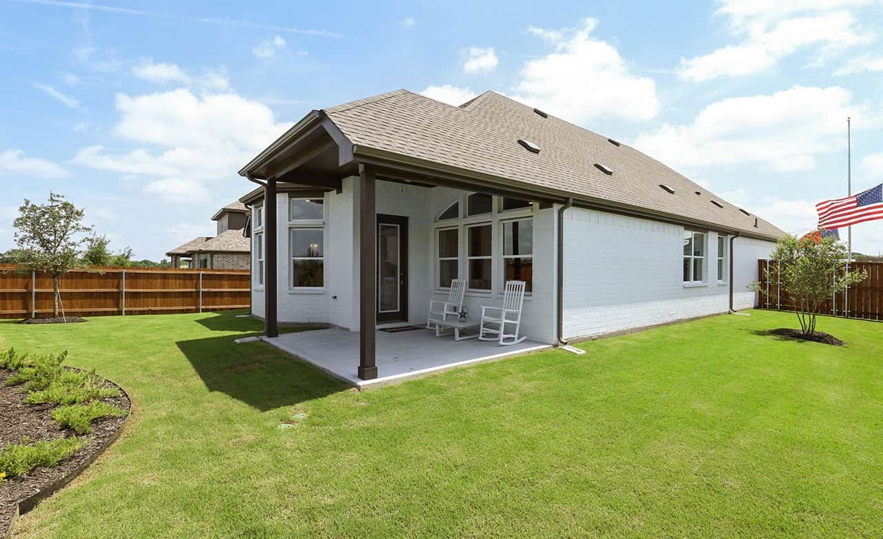 Modern white brick house with covered porch, green lawn, wooden fence, blue sky; Thompson Farms.