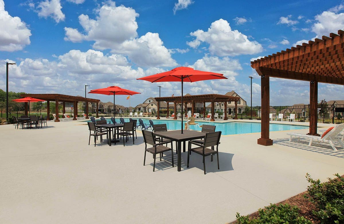 Outdoor pool area with red umbrellas, wooden pergolas, luxury seating at Thompson Farms community.