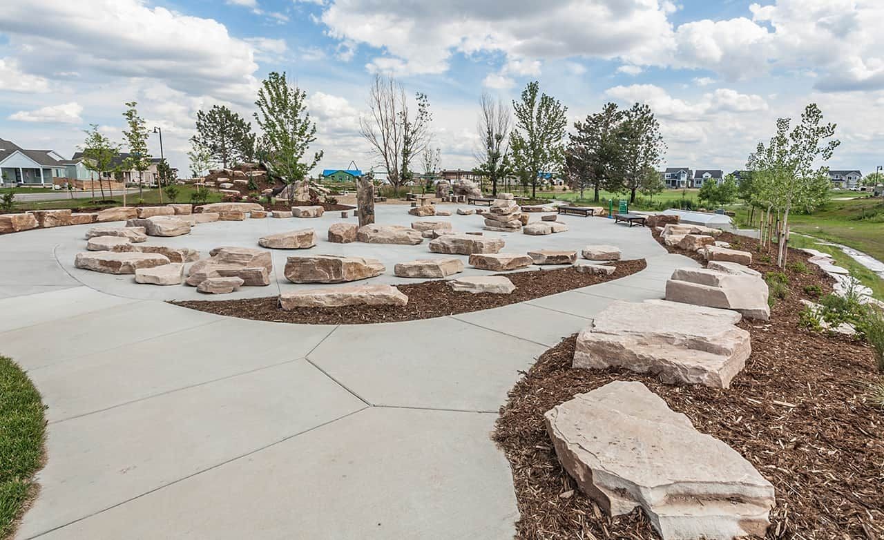 Community park with natural stone seating and pathways in Trailside on Harmony, Colorado. Scenic landscaping enhances charm.