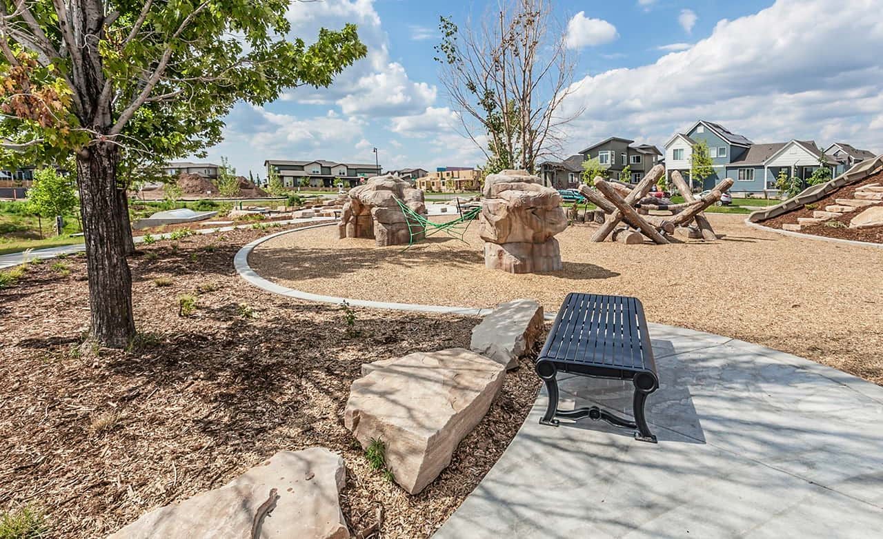 Park area with modern play structures and pathway in Trailside on Harmony, surrounded by residential homes.