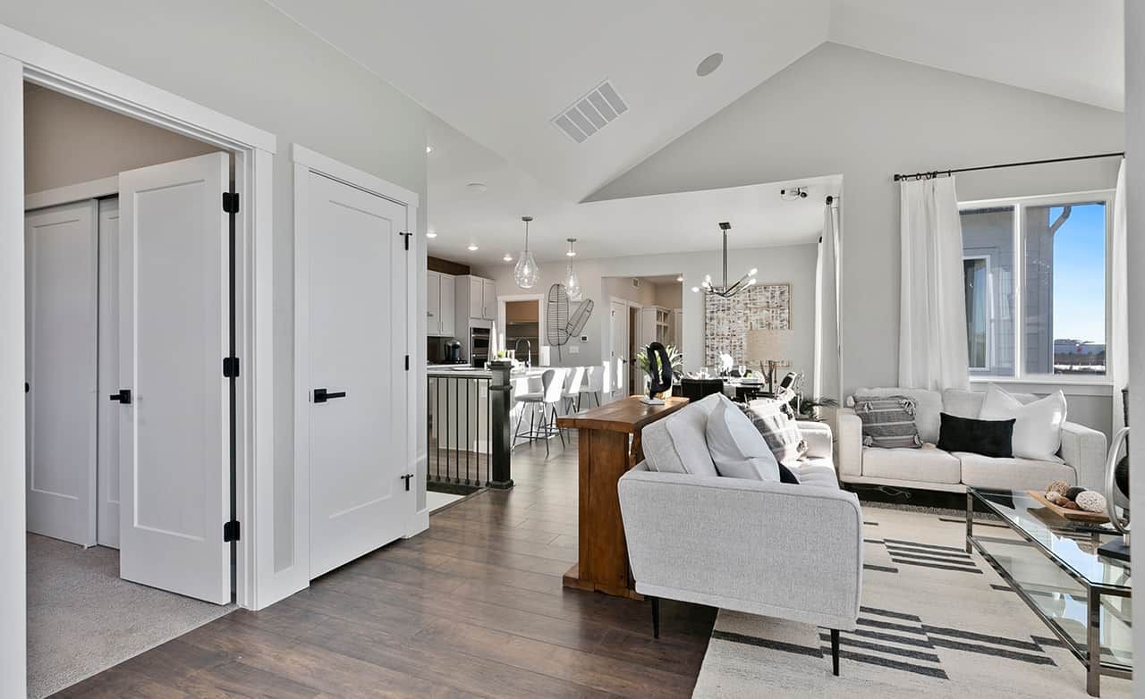 Modern living room with vaulted ceiling, hardwood floors, large windows, and pendant lighting in Trailside on Harmony.