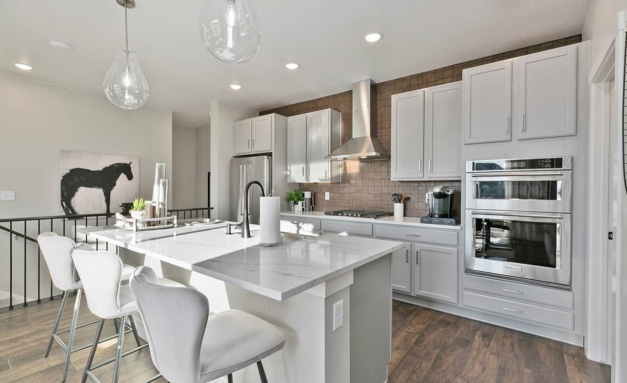 Modern kitchen with marble island, pendant lights, stainless steel appliances, and wall art in Trailside on Harmony.