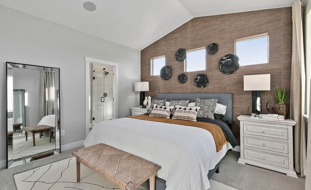 Modern bedroom with textured accent wall, elegant decor, and en-suite bathroom in Trailside on Harmony.