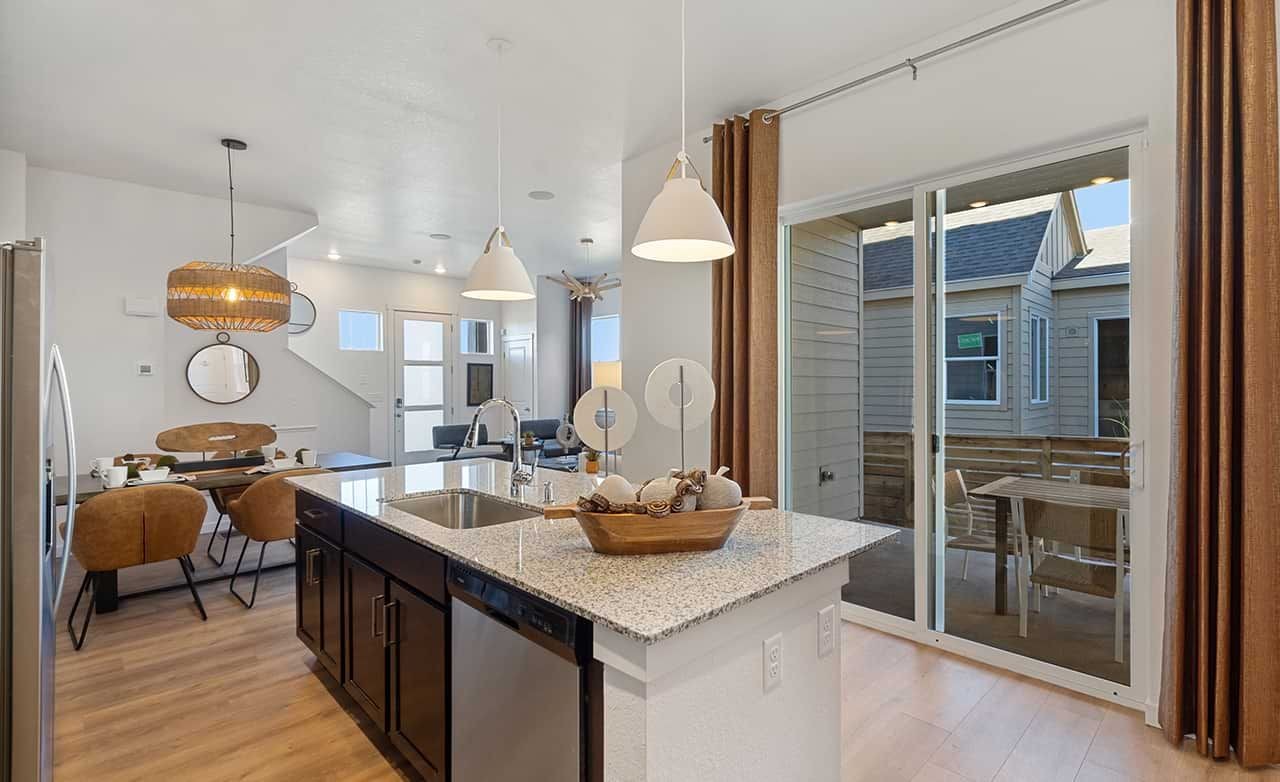 Modern kitchen with granite island, pendant lights, in Trailside on Harmony. View of patio through glass door.