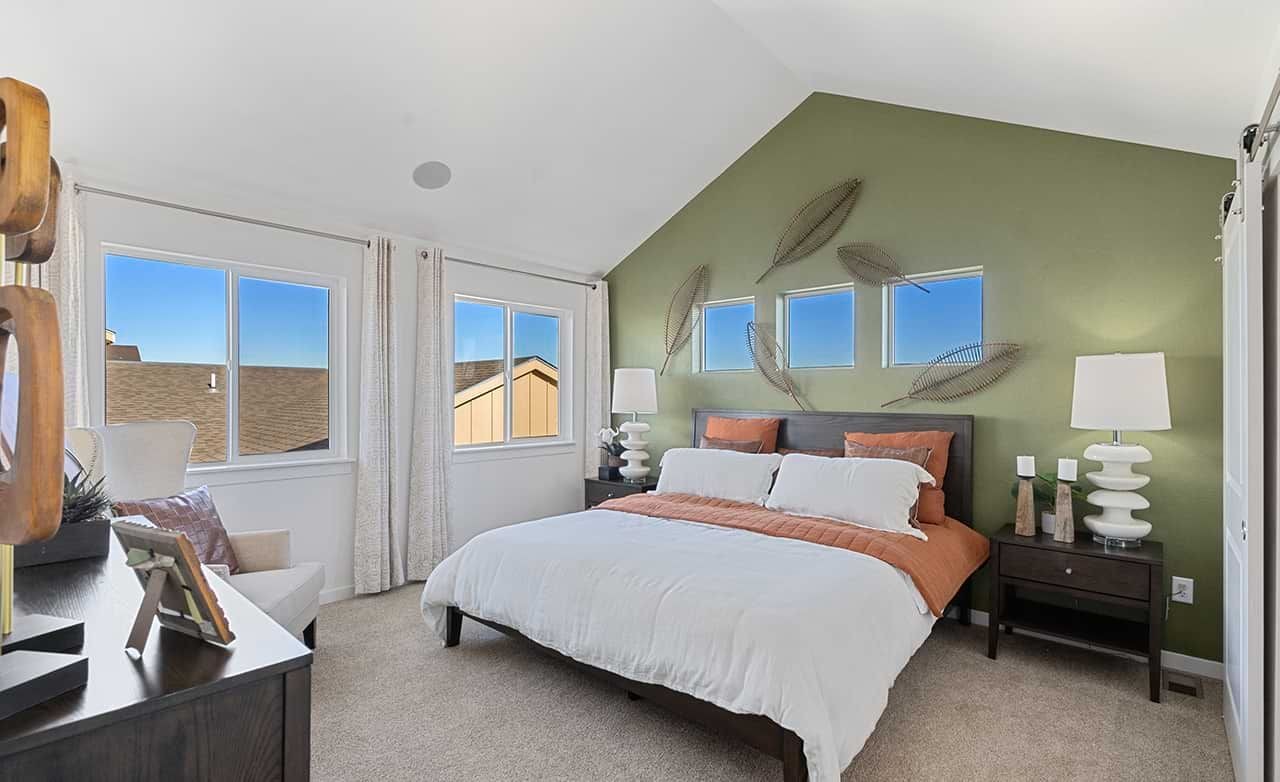 Elegant bedroom with vaulted ceiling, green accent wall, and modern decor in Trailside on Harmony community.